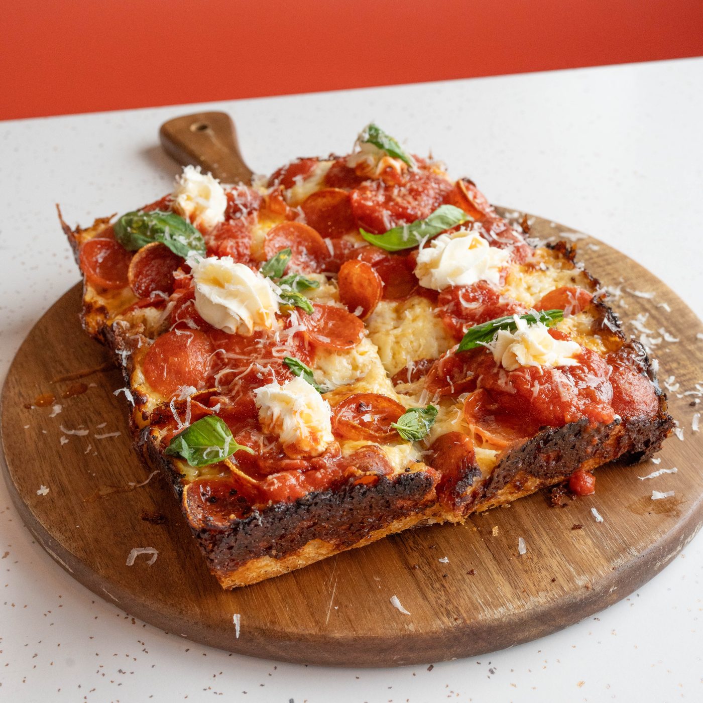 The Usual: a Detroit-style pepperoni pizza with hot honey, whipped ricotta, and basil, showing the dark caramelized cheese edge