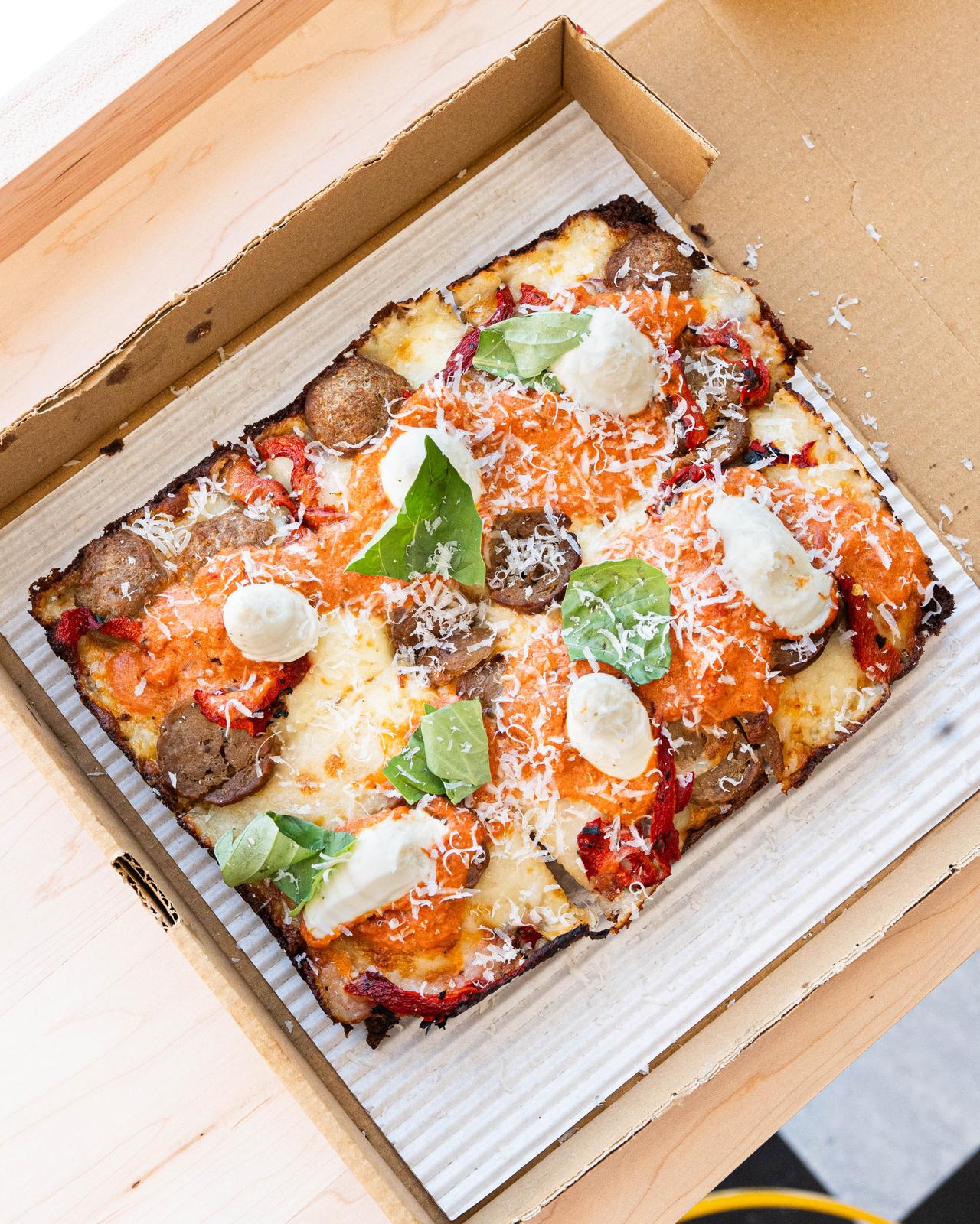 A whole Oh, My Meatball! pizza in an open box, seen from above, with sliced meatballs, vodka sauce, whipped ricotta, roasted peppers, and basil